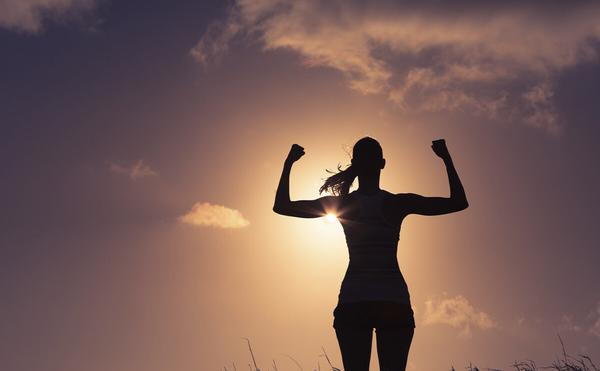 A silhouetted figure of a person standing with arms raised triumphantly against a sunset background, symbolizing empowerment and achievement.