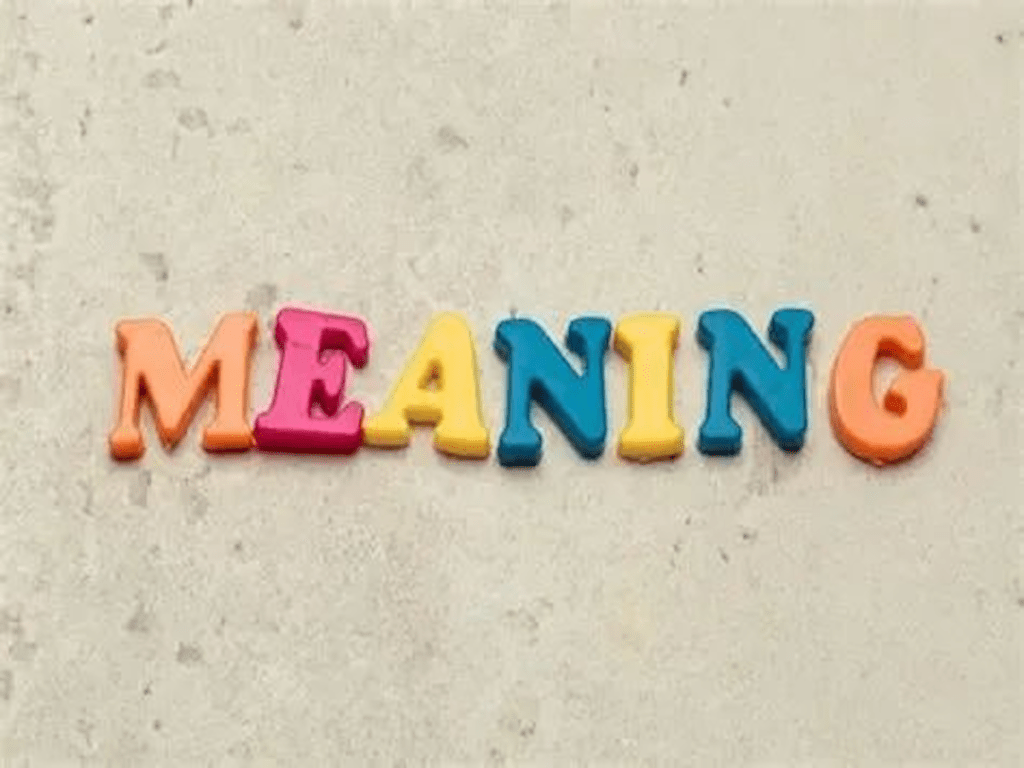 字母积木拼出 "MEANING" 一词，背景为简单的灰色表面。